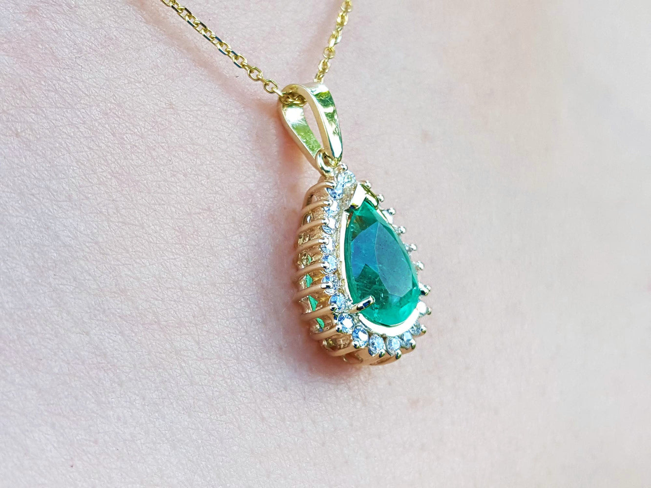 Gold pendant with a natural teardrop-shaped emerald on a light pink skin background