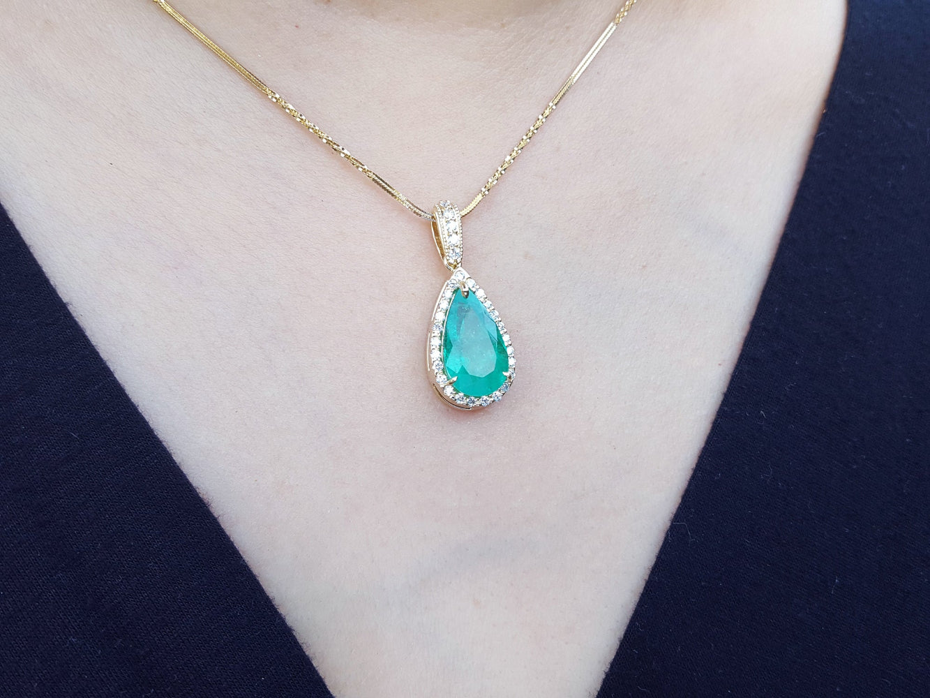Teardrop-shaped natural emerald pendant on a gold chain on a woman&#39;s neck