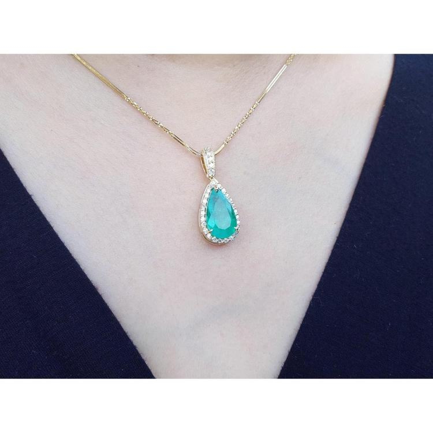 18K yellow gold teardrop emerald pendant with halo diamonds on a delicate chain, worn on a neck.