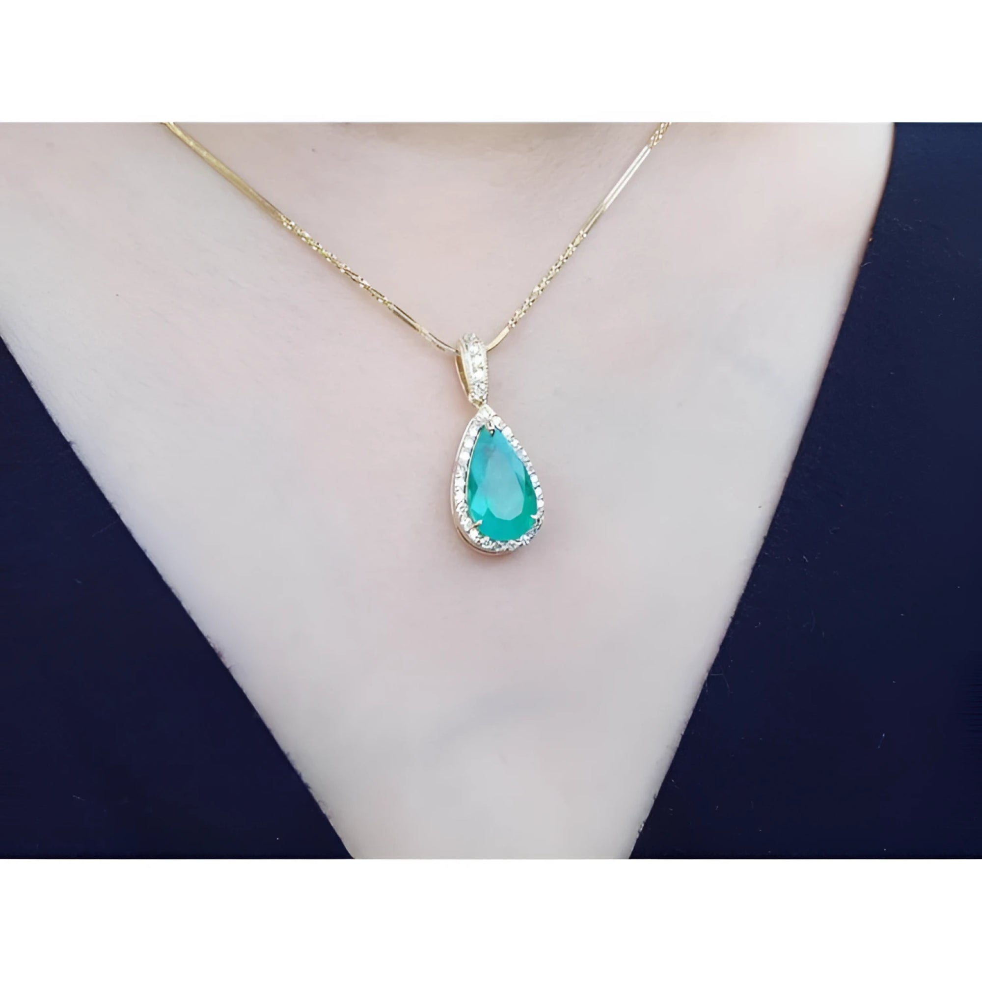 18K yellow gold teardrop emerald pendant with halo diamonds on a delicate chain, worn on a neck.