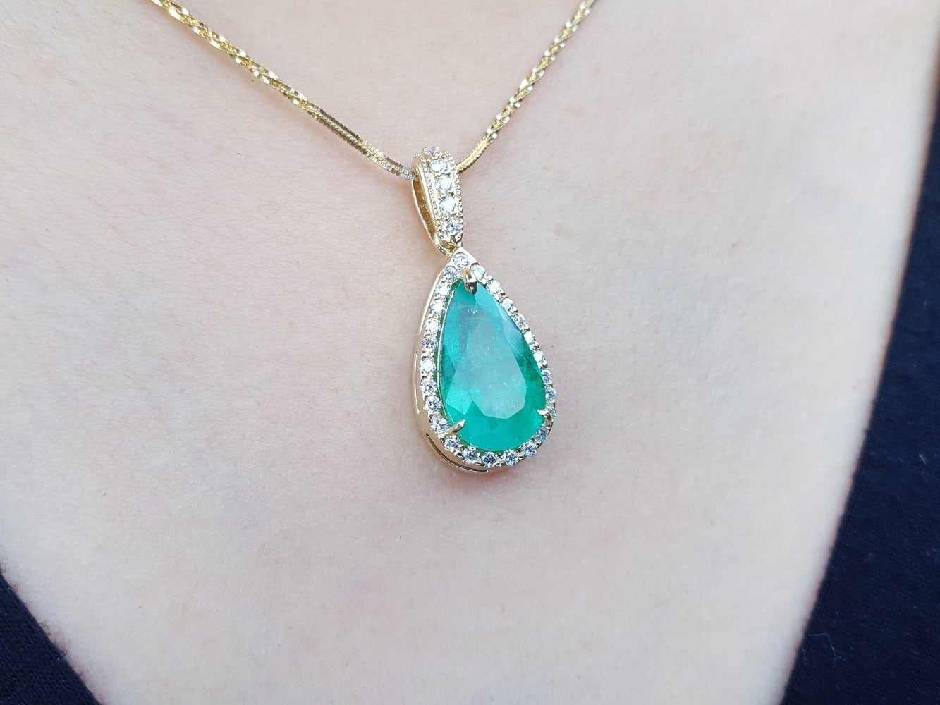 Teardrop-shaped genuine colombian emerald pendant on a gold chain against a skin background