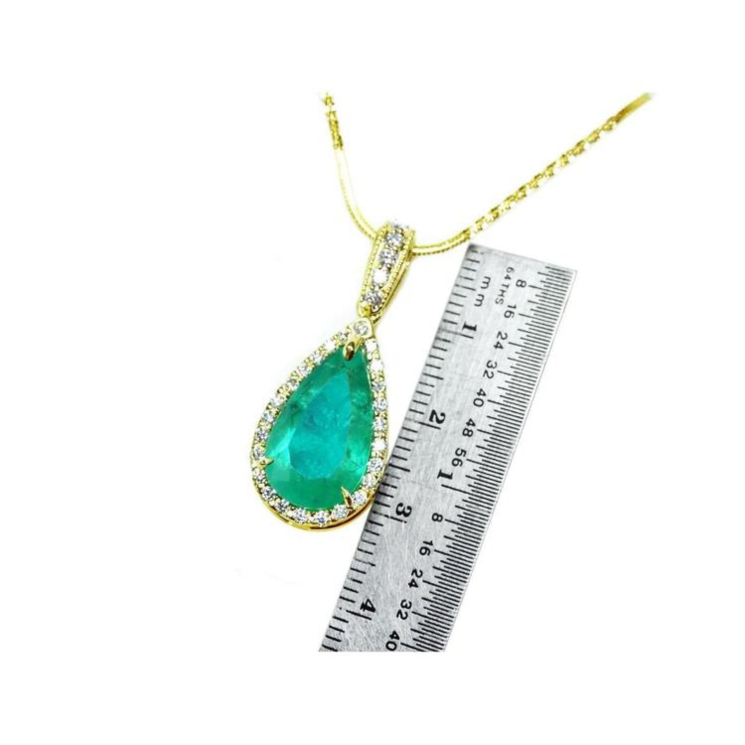 A natural colombian emerald teardrop pendant on a gold chain with a ruler for scale on a white background