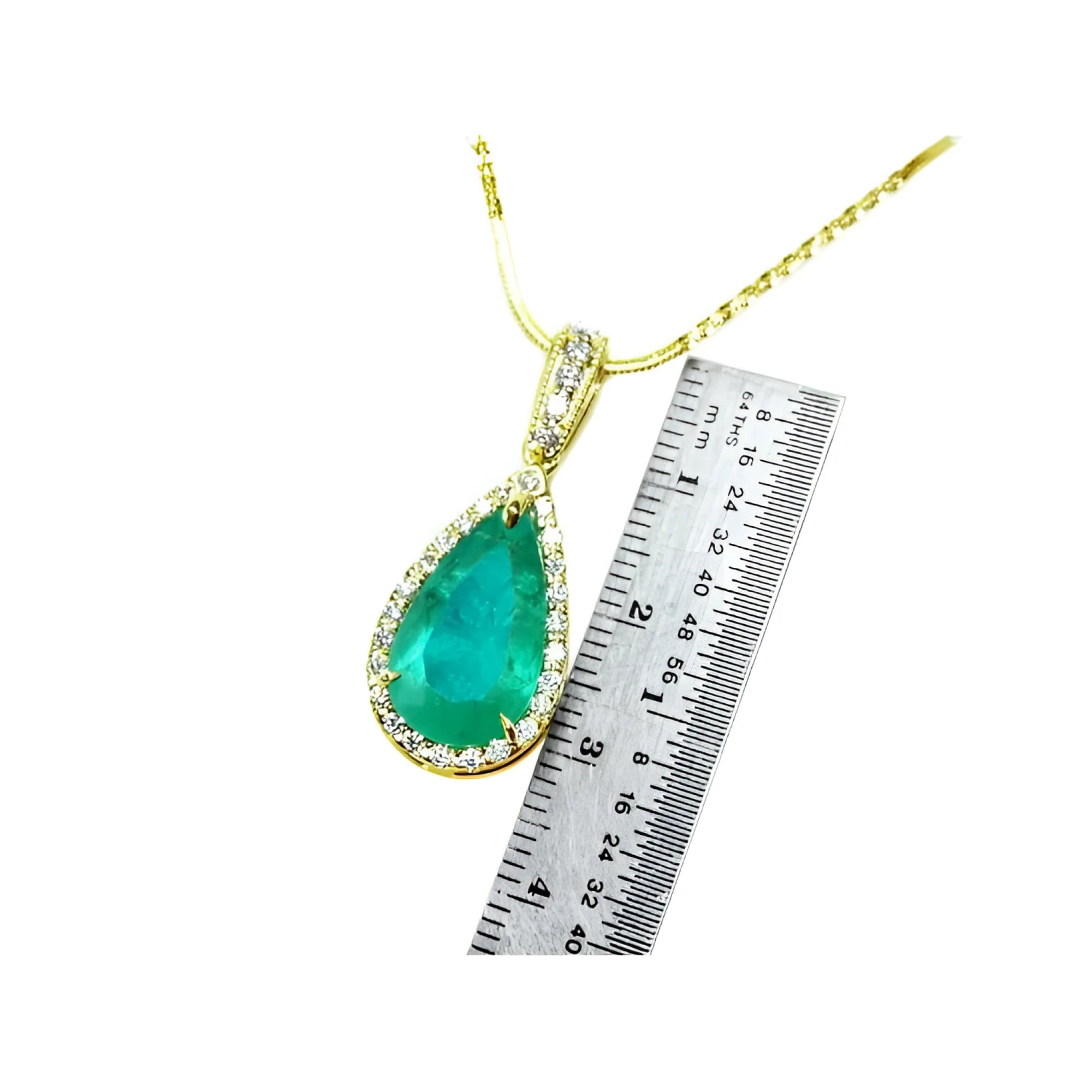 A natural colombian emerald teardrop pendant on a gold chain with a ruler for scale on a white background