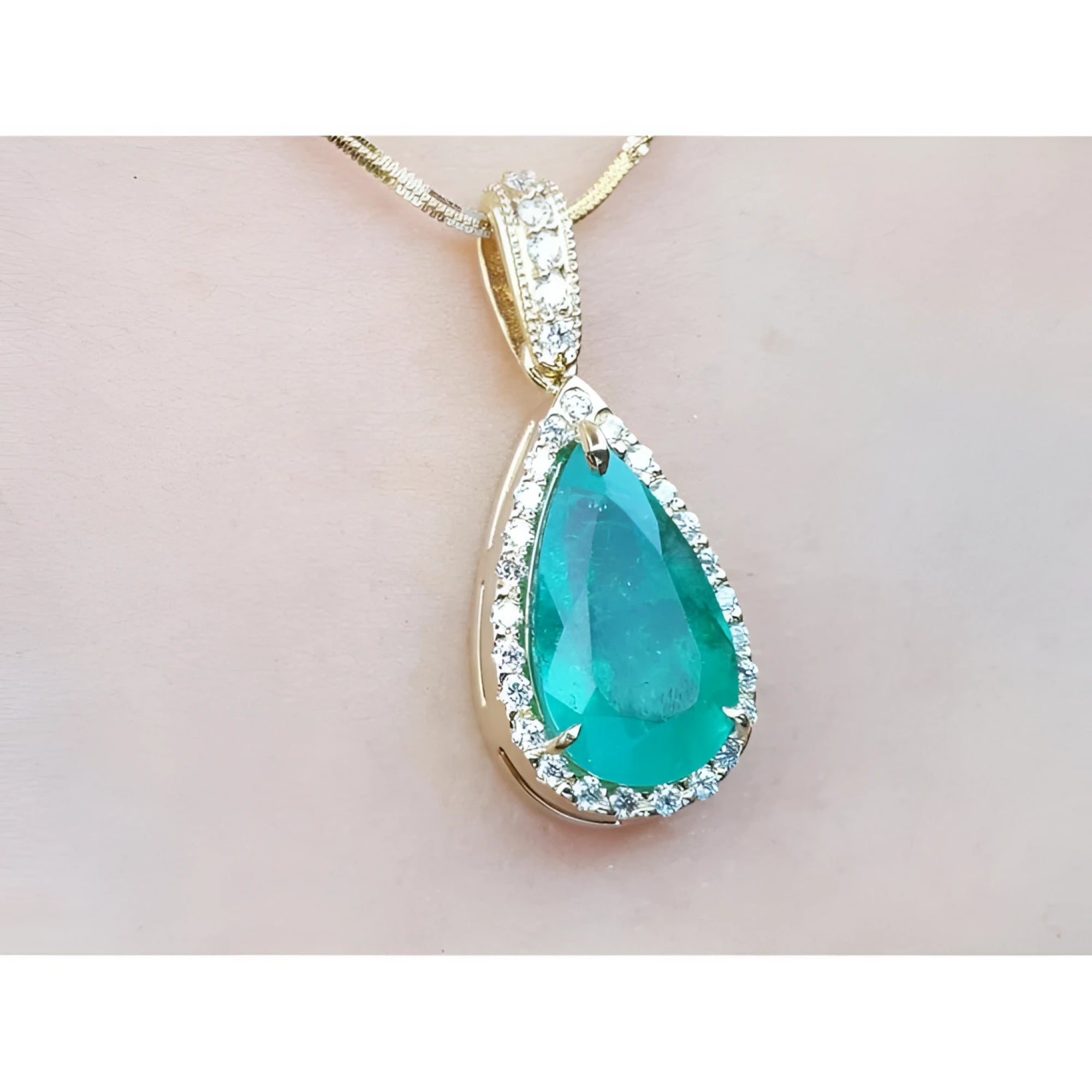 Teardrop-shaped emerald gemstone pendant with halo diamond accents on a light pink skin background