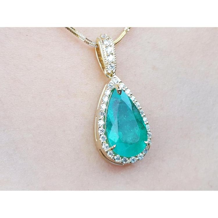 Teardrop-shaped emerald gemstone pendant with halo diamond accents on a light pink skin background