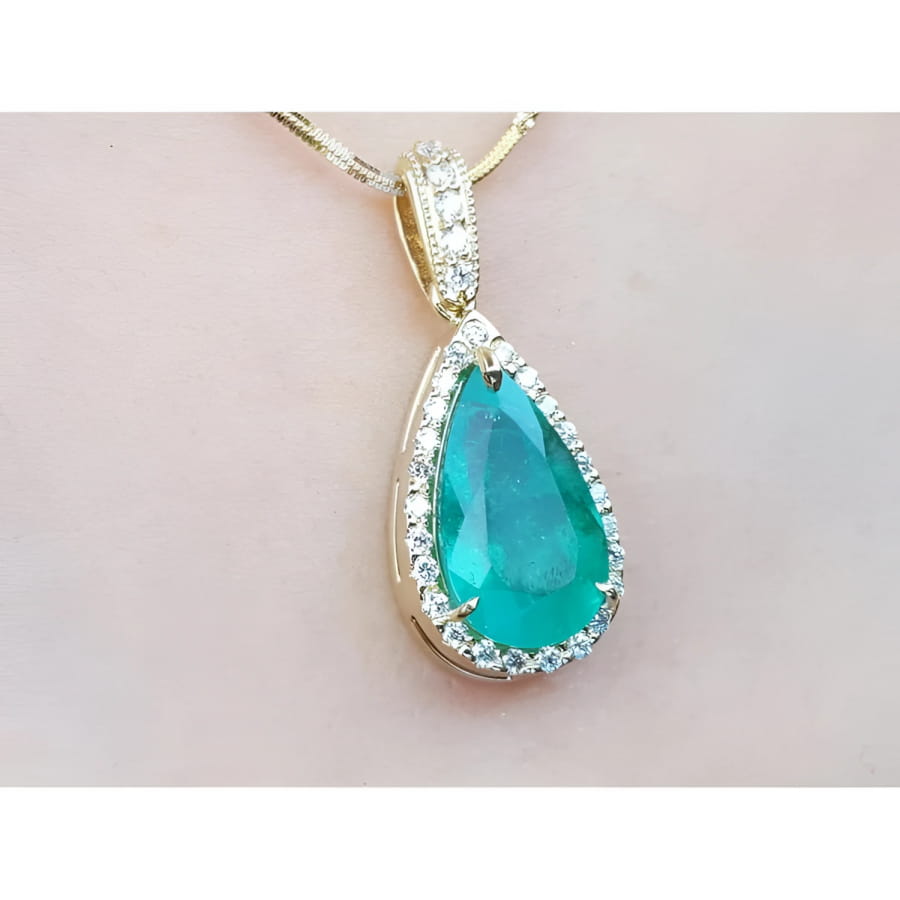 Teardrop-shaped emerald gemstone pendant with halo diamond accents on a light pink skin background