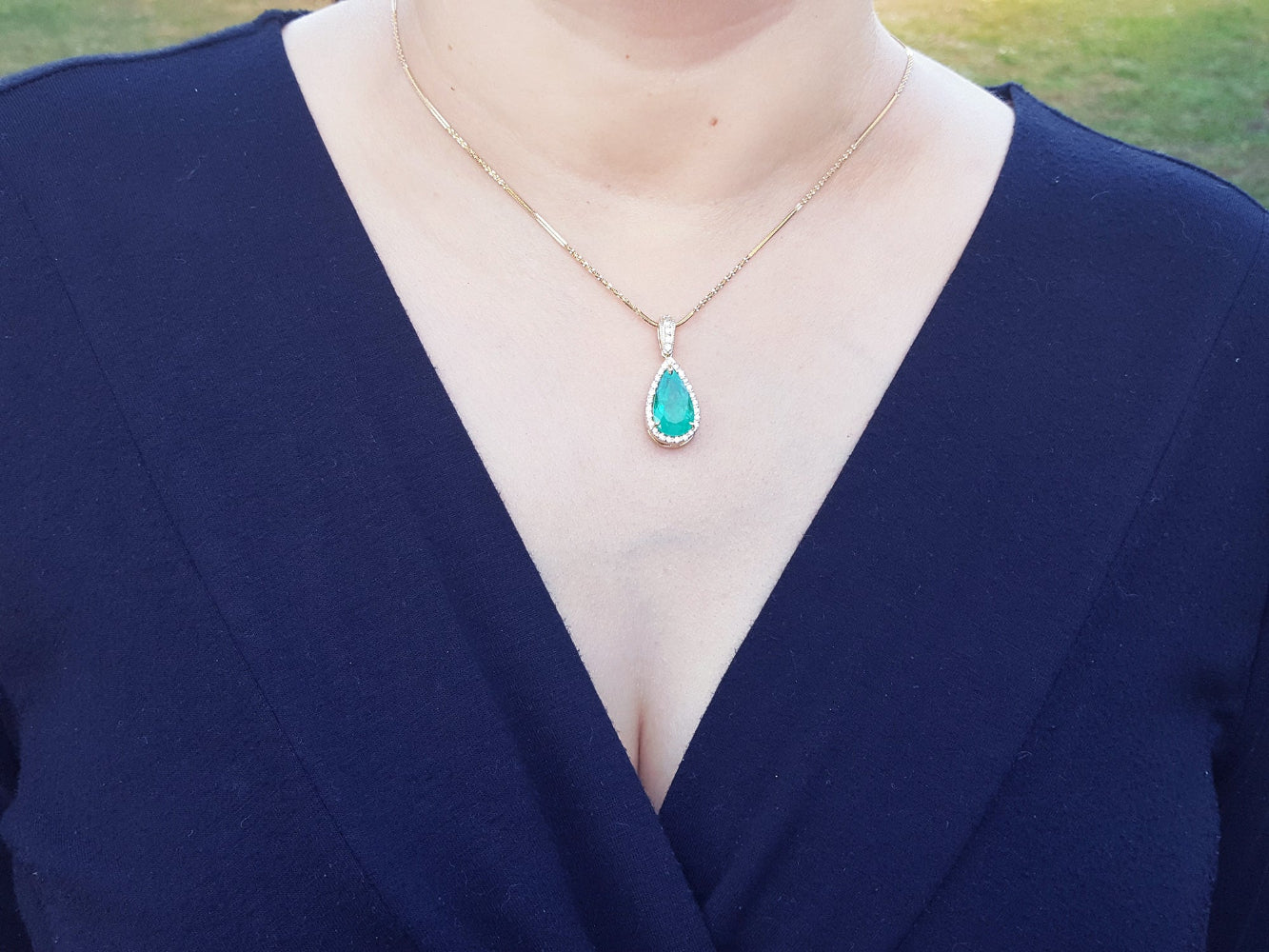 A natural Muzo mine colombian emerald teardrop pendant necklace on a woman wearing a navy-blue top.