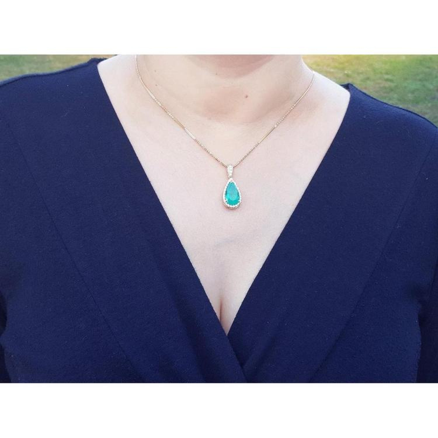 18K yellow gold teardrop emerald pendant with halo diamonds on a woman's neck.