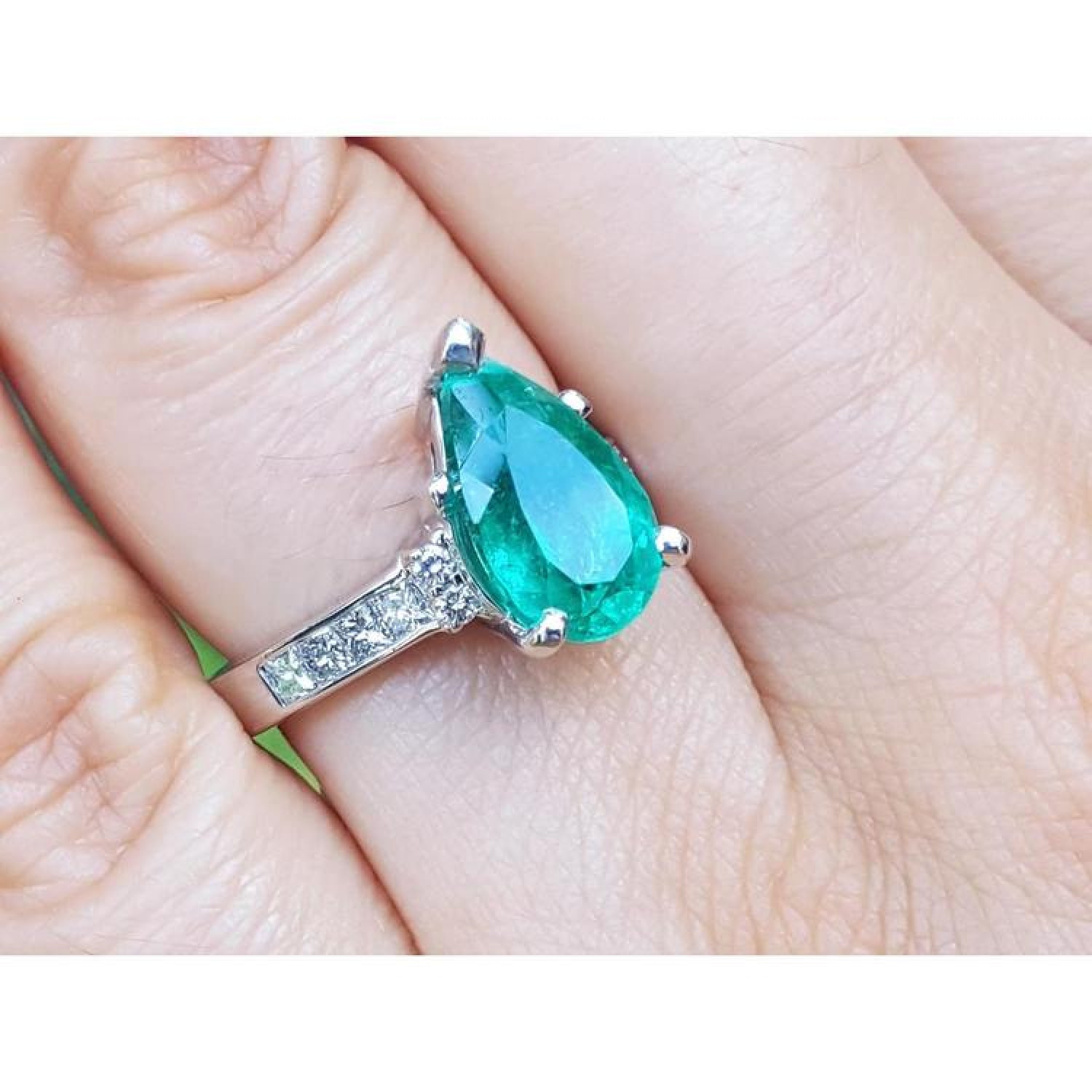 3.09 ct pear-shaped deep bluish-green emerald ring with princess cut diamonds in 14K white gold.