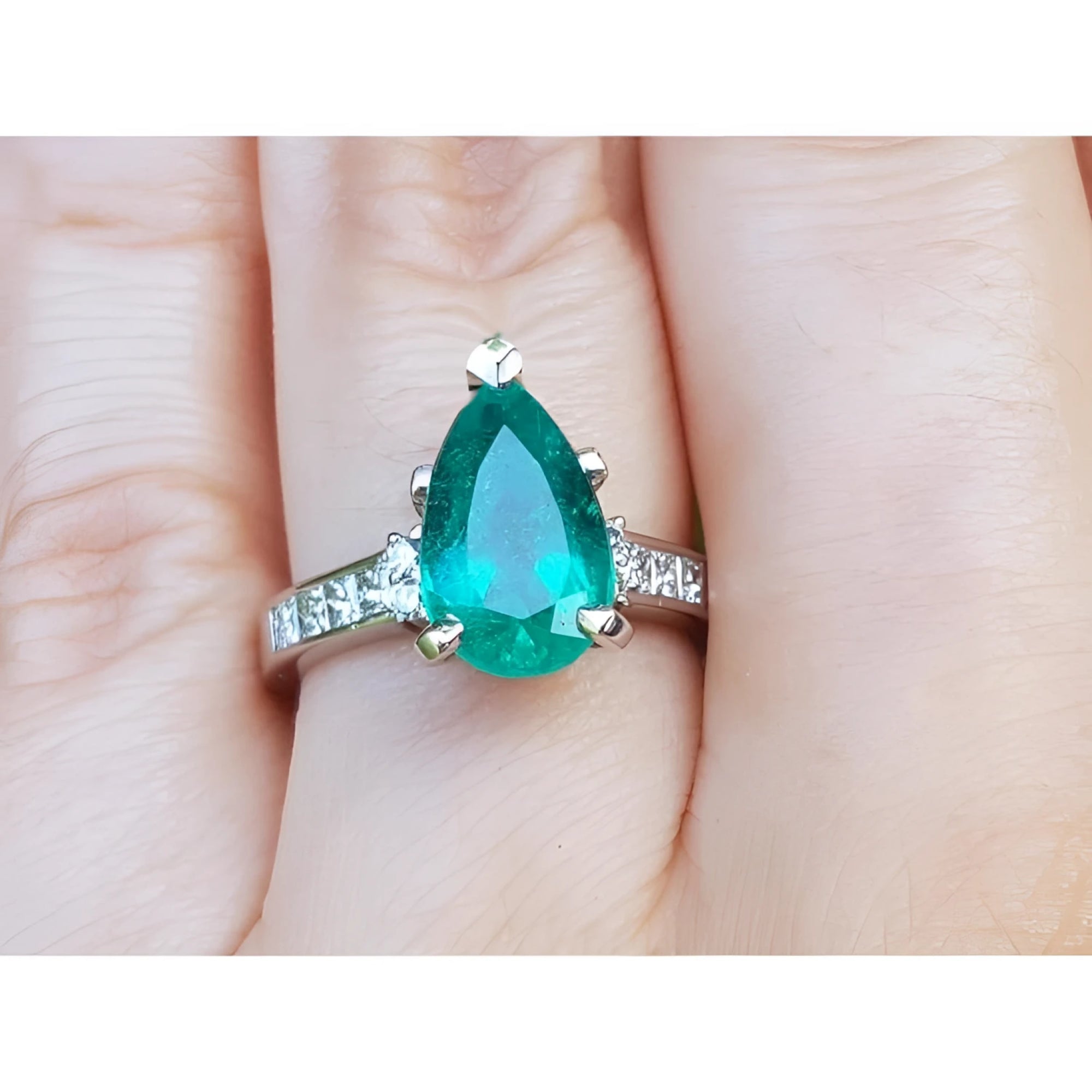 A Colombian emerald teardrop ring and princess cut band diamonds on a hand.