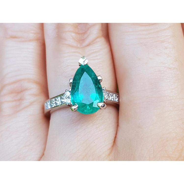 A Colombian emerald teardrop ring and princess cut band diamonds on a hand.