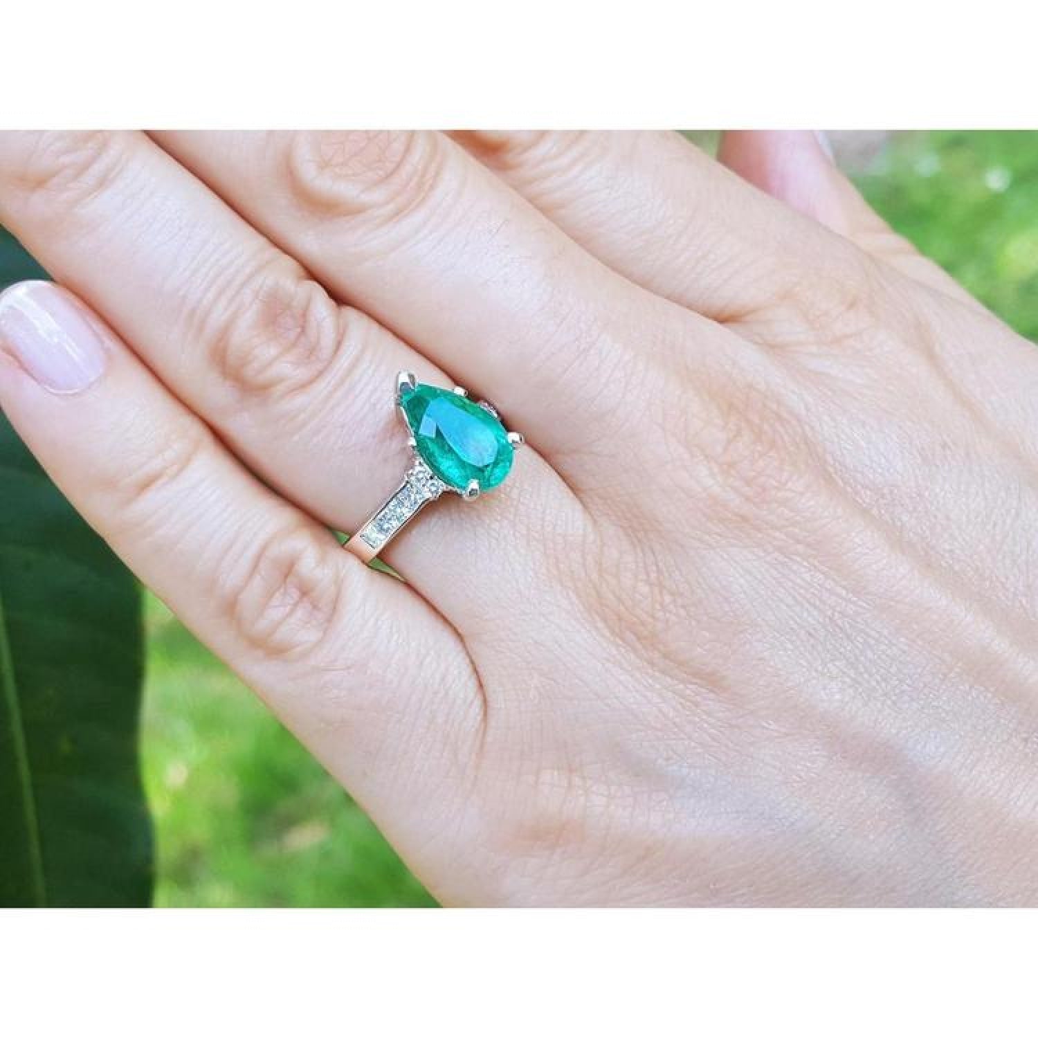 Pear-shaped emerald ring with princess cut diamonds on a 14K white gold band, worn on a hand.