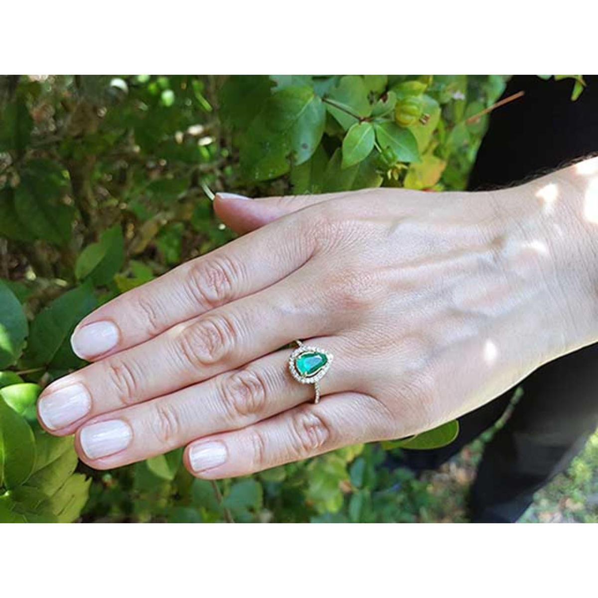 Hand wearing a teardrop emerald ring against a natural background.