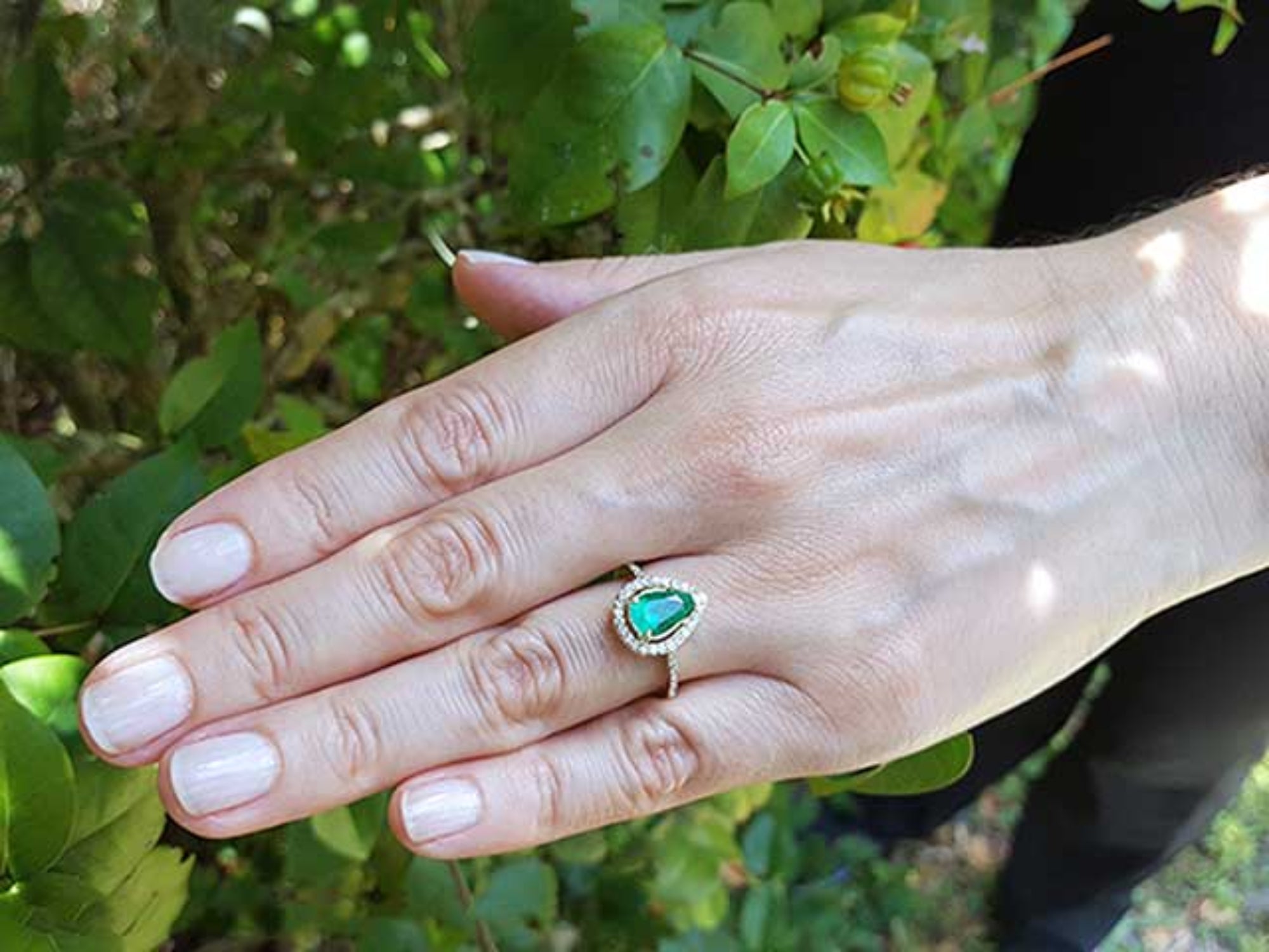 Hand wearing a teardrop emerald ring against a natural background.