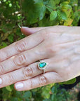 Hand wearing a teardrop emerald ring against a natural background.