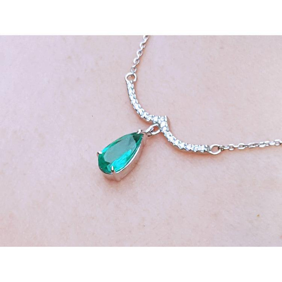 White gold necklace with a pear-shaped emerald and diamond-studded wavy bar.