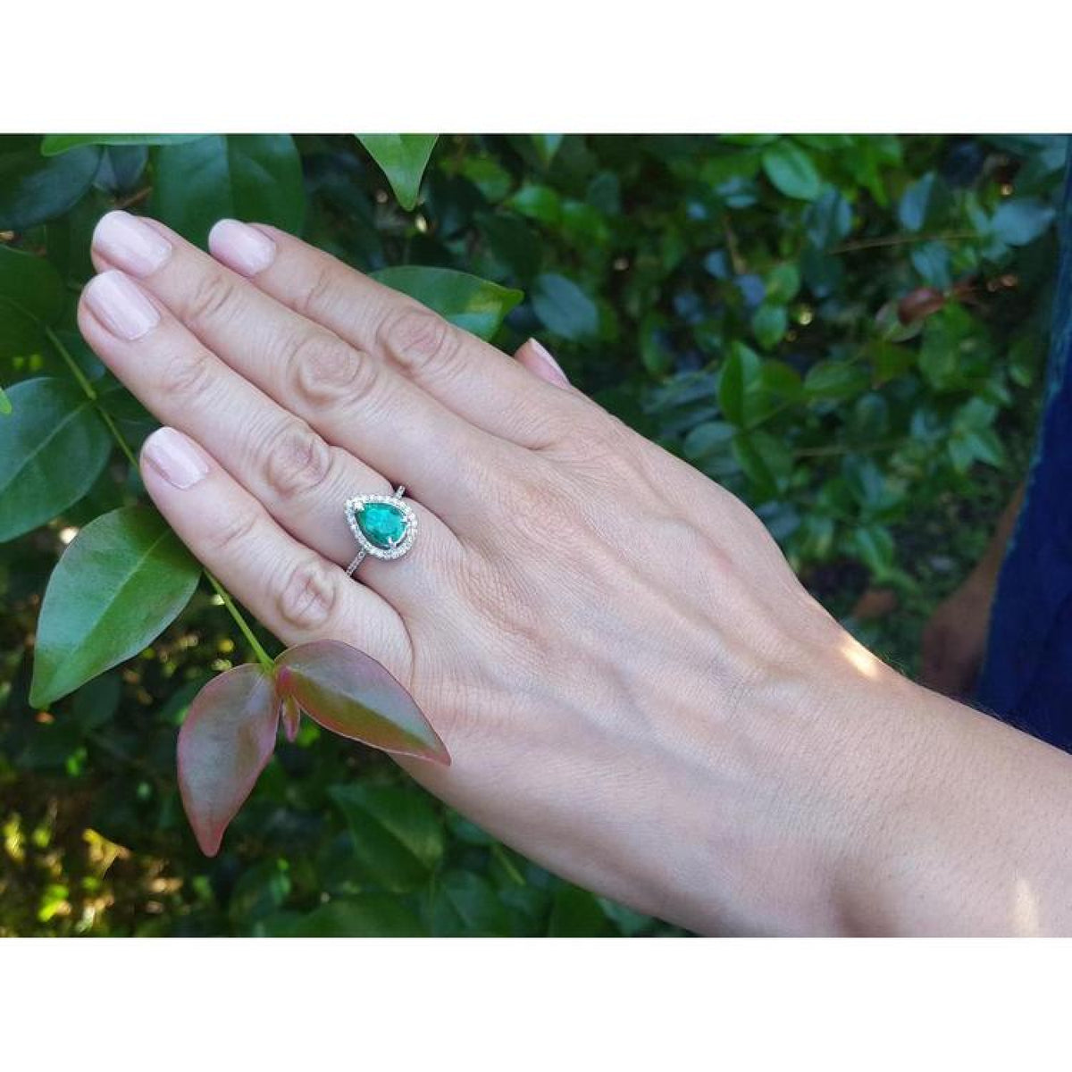 1.39 ct. teardrop emerald halo ring with diamonds on a 14K white gold band, worn on a hand.