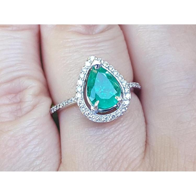 A natural colombian emerald teardrop ring with diamond halo on a finger.