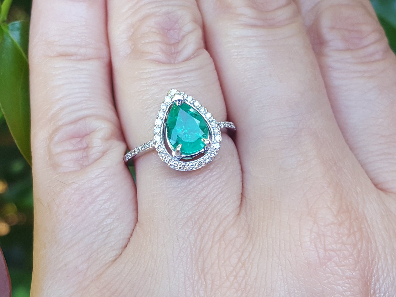Ring with a natural pear shaped emerald on a person&#39;s finger against a blurred natural background.