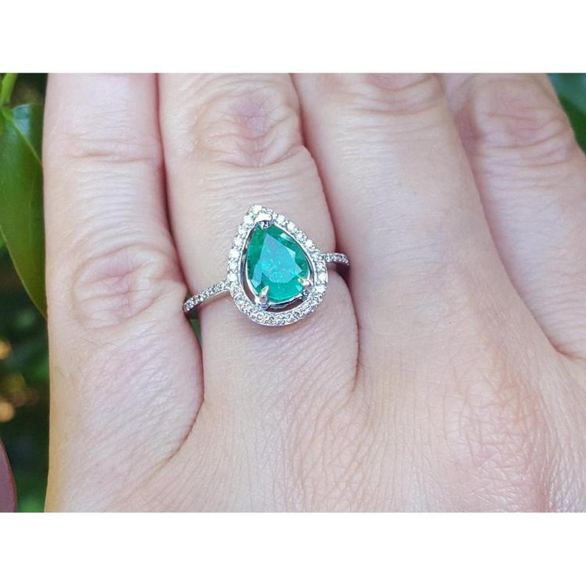 Teardrop emerald ring in 14K white gold with a diamond halo, worn on a finger.
