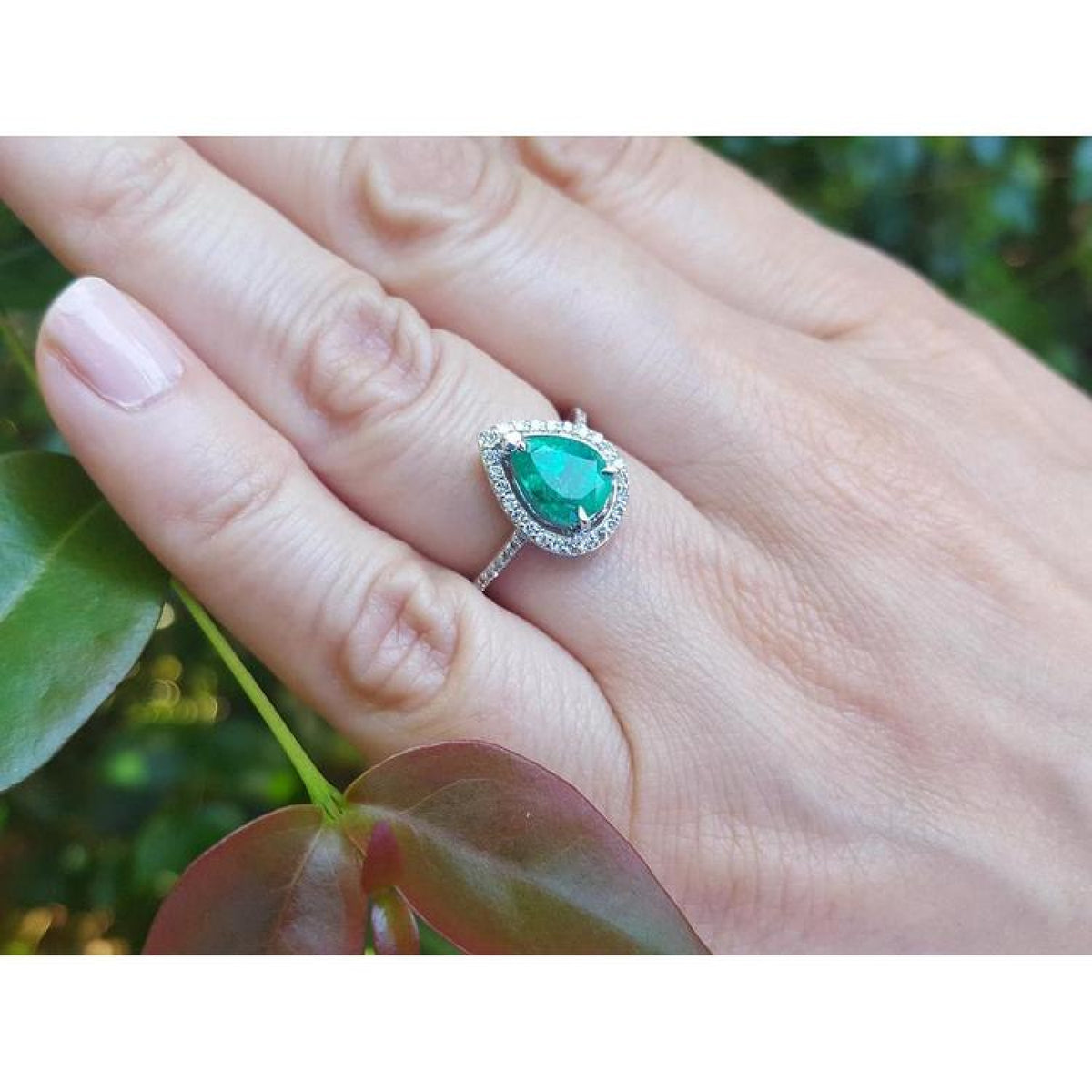 Teardrop emerald halo ring with diamonds on a hand, 14K white gold.