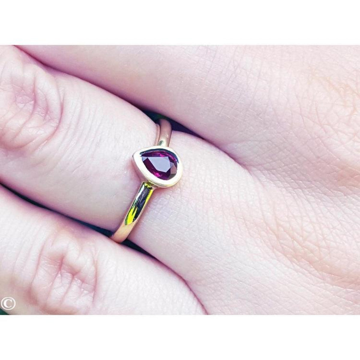 Woman's hand wearing a 14K yellow gold ring with a teardrop natural ruby solitaire.
