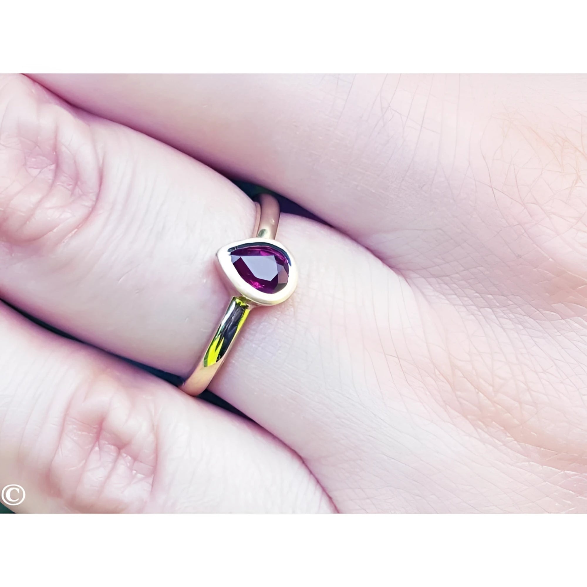 Woman's hand wearing a 14K yellow gold ring with a teardrop natural ruby solitaire.
