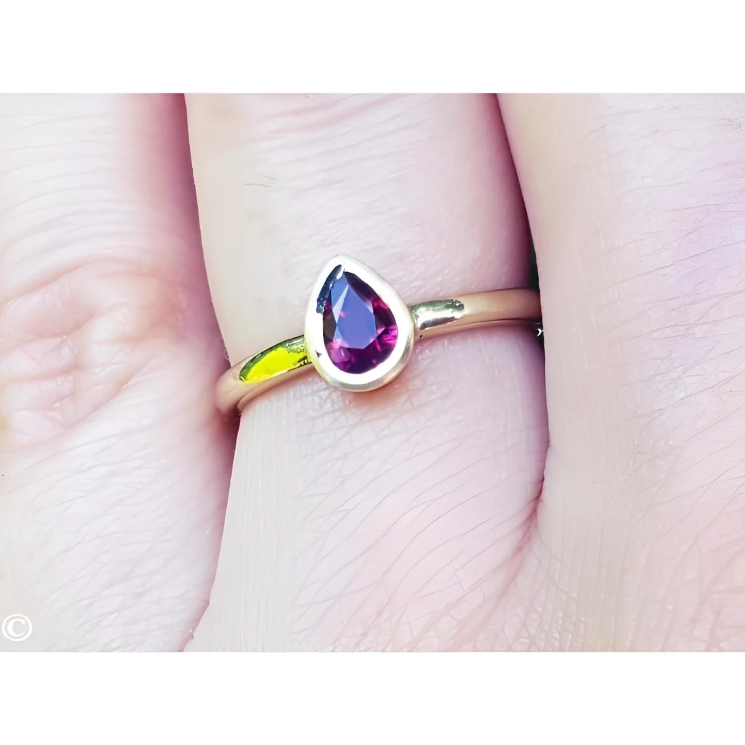 Woman's hand wearing a 14K yellow gold ring with a bezel-set teardrop natural ruby solitaire.