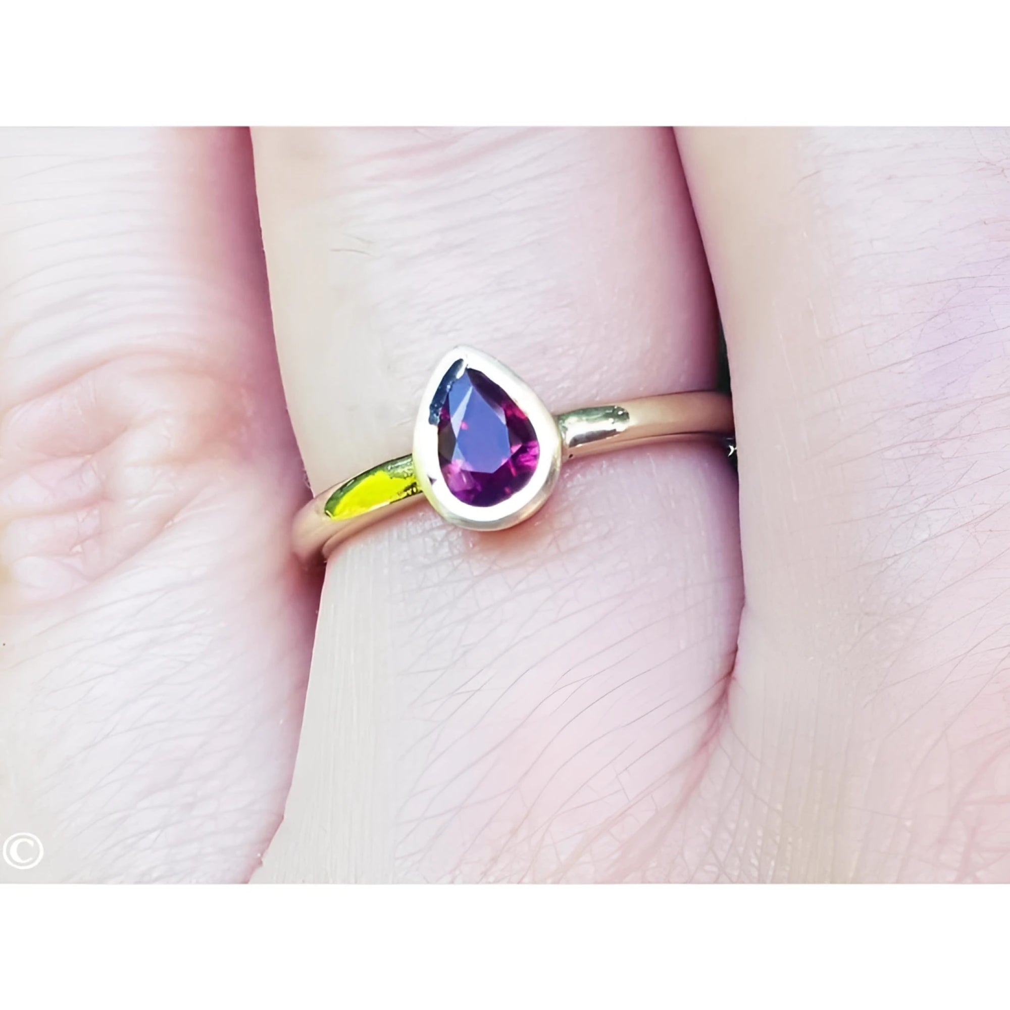Woman's hand wearing a 14K yellow gold ring with a bezel-set teardrop natural ruby solitaire.