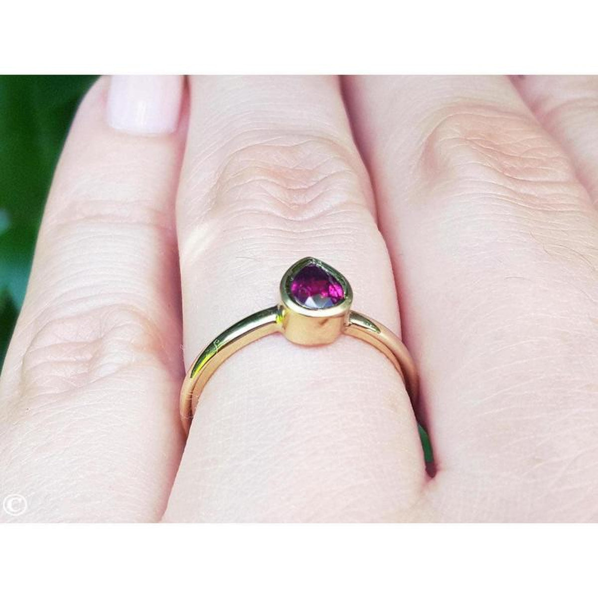 Woman's hand wearing a 14K yellow gold ring with a bezel-set teardrop natural ruby solitaire.