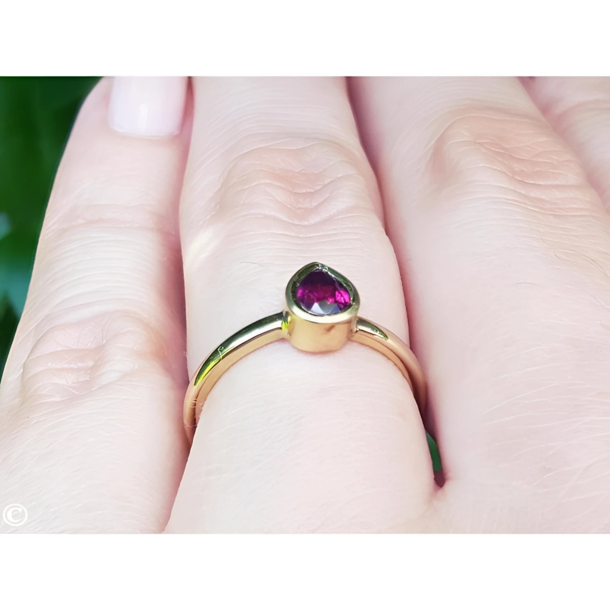 Woman's hand wearing a 14K yellow gold ring with a bezel-set teardrop natural ruby solitaire.
