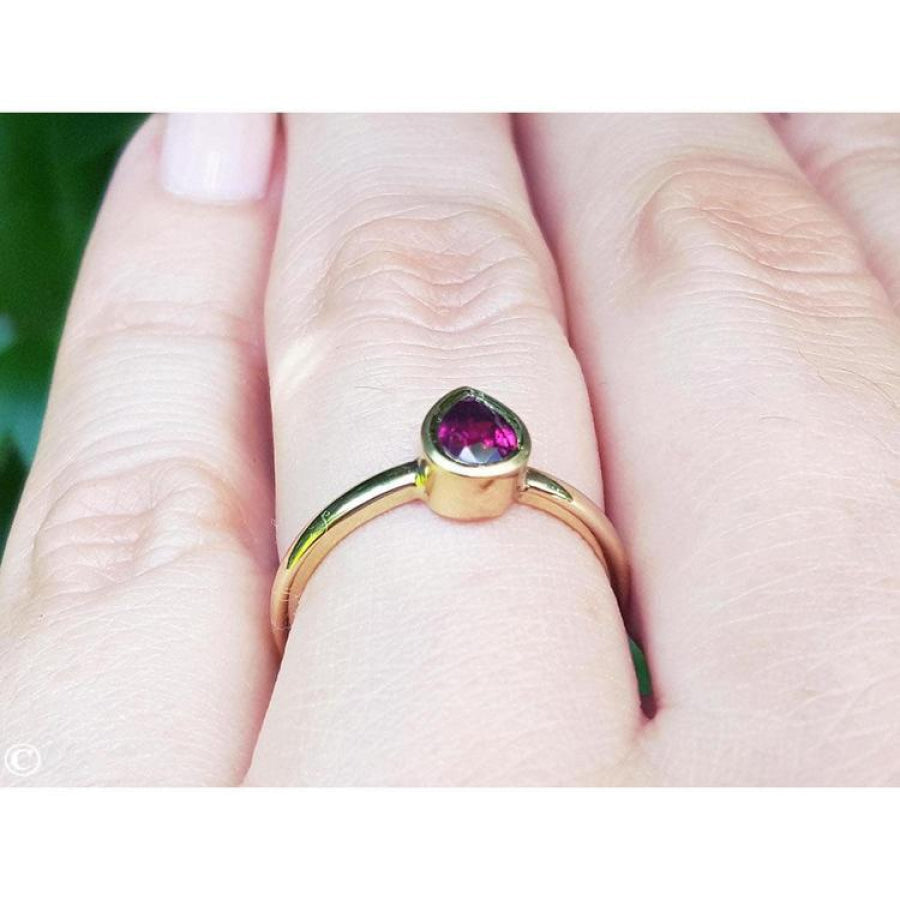 Woman's hand wearing a 14K yellow gold ring with a bezel-set teardrop natural ruby solitaire.