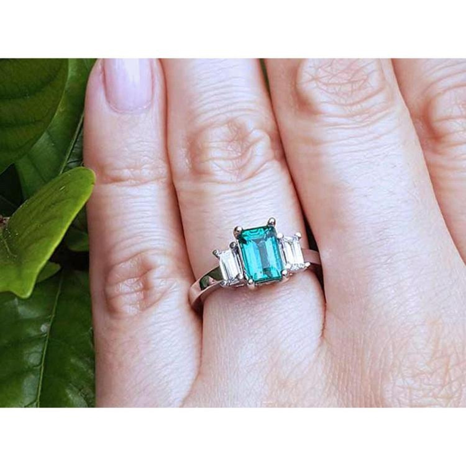 Emerald cut three stone ring with medium bluish green emerald and side baguette diamonds in 18k white gold.