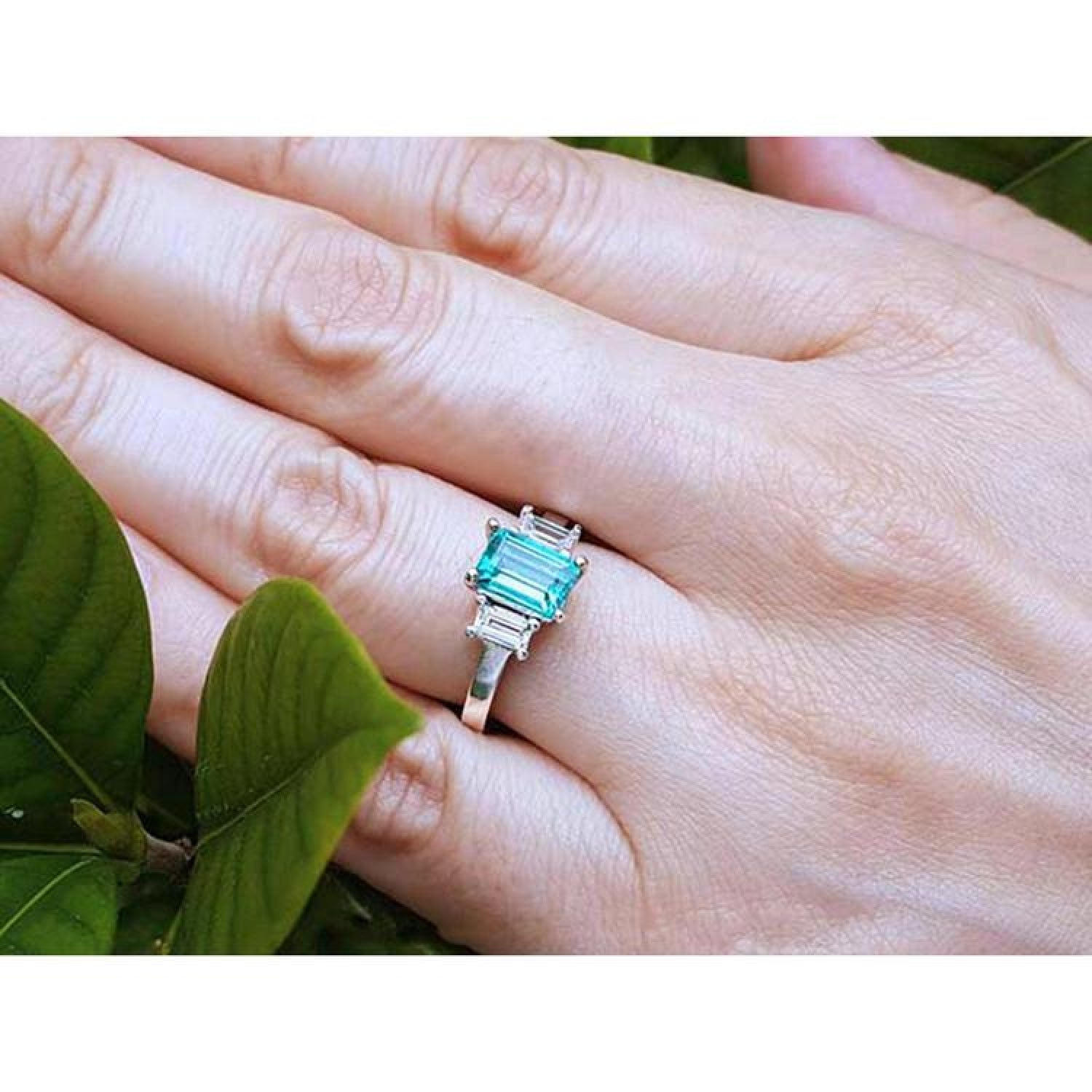 Emerald cut three stone ring with medium bluish green emerald and side baguette diamonds in 18k white gold.