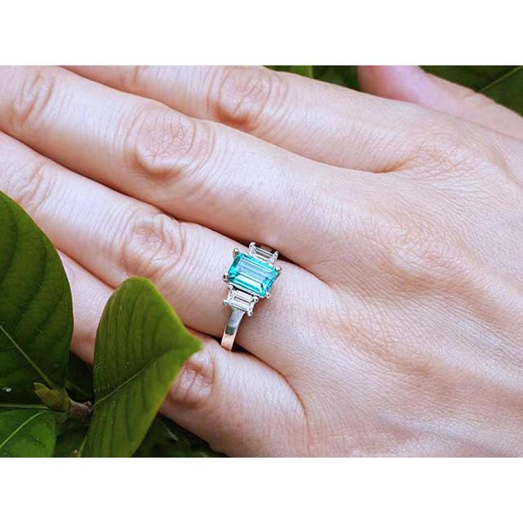 Emerald cut three stone ring with medium bluish green emerald and side baguette diamonds in 18k white gold.