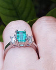 An emerald and baguette diamond rings for women on a finger against a natural background.