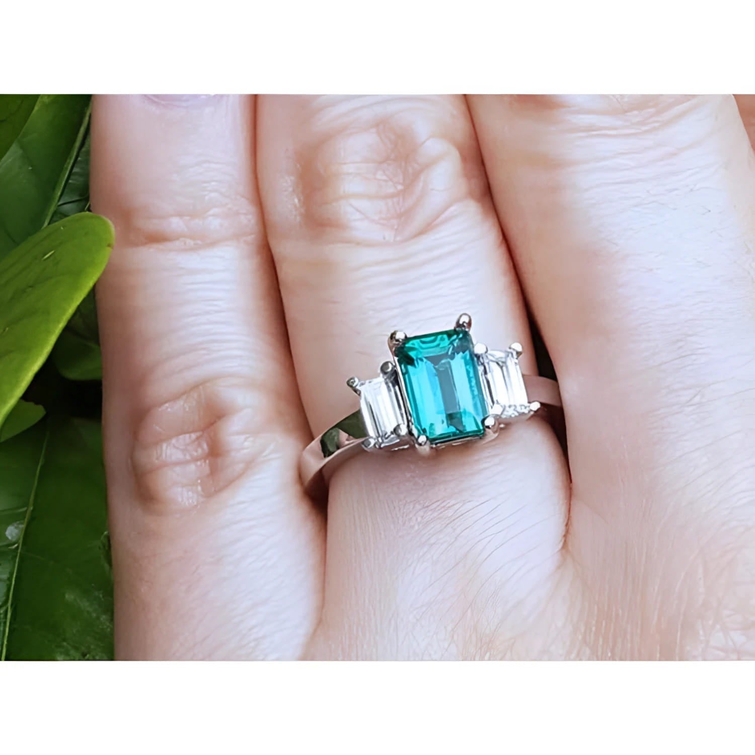 A three stone emerald and side straight baguettes diamond ring crafted in 18k white gold.