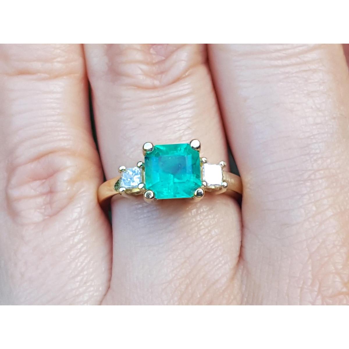 A three stone emerald engagement rings with a green gemstone on a finger.