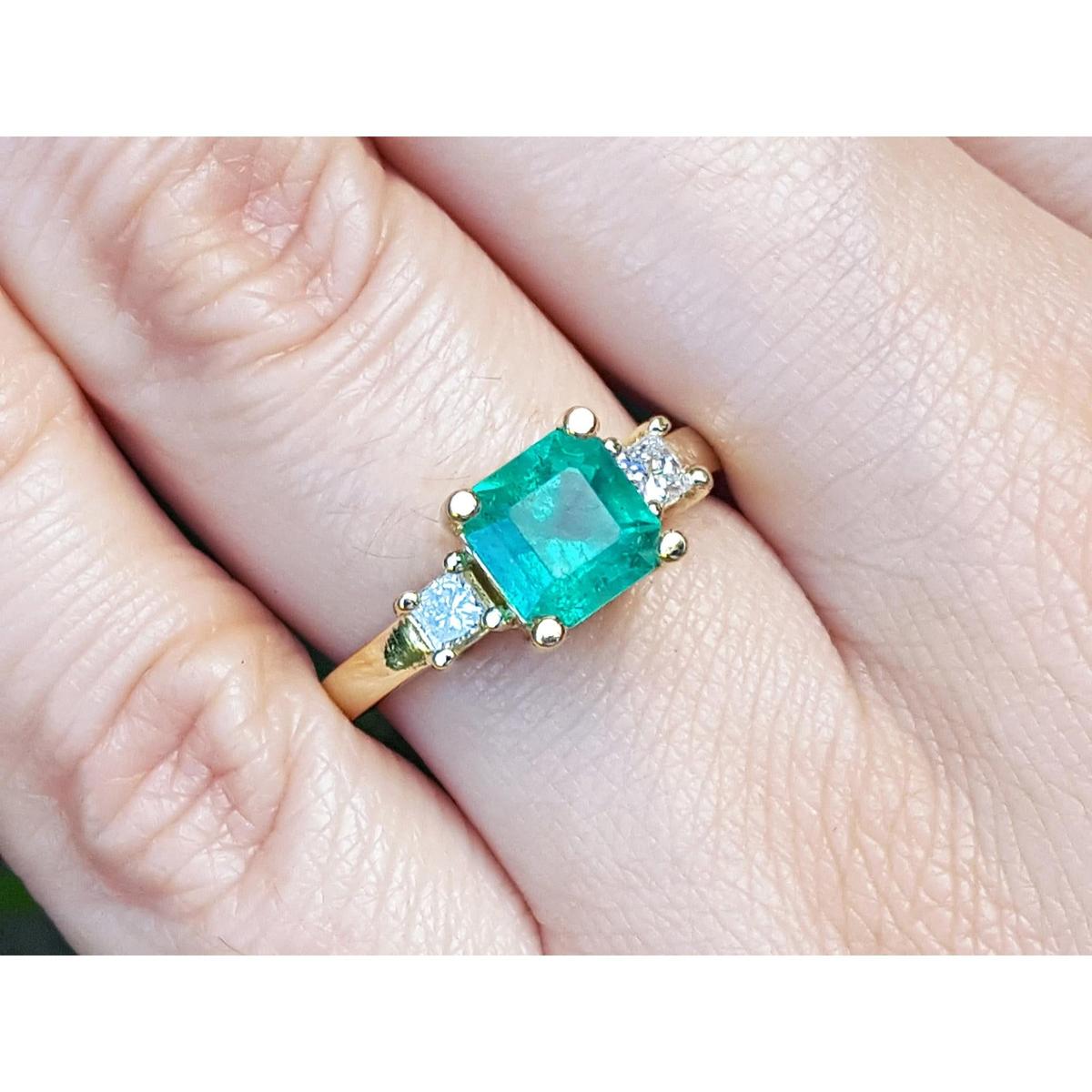 Emerald ring with gold setting and side diamonds on a finger.