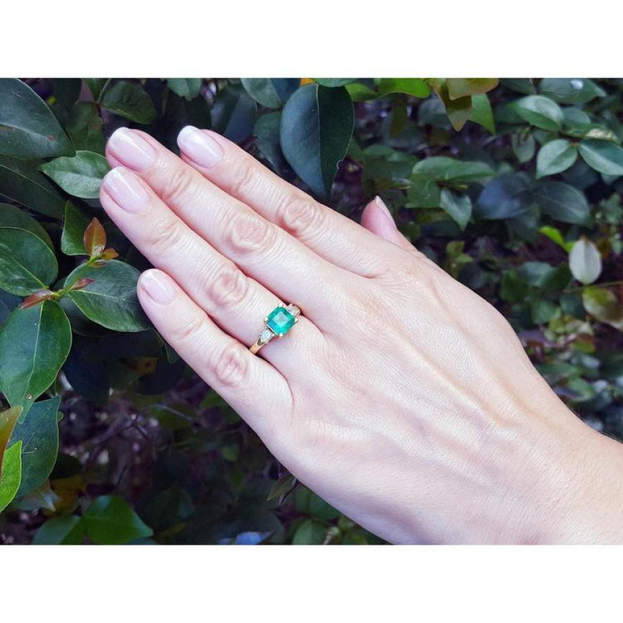 18K yellow gold three-stone ring with a square emerald and princess-cut side diamonds on a hand.
