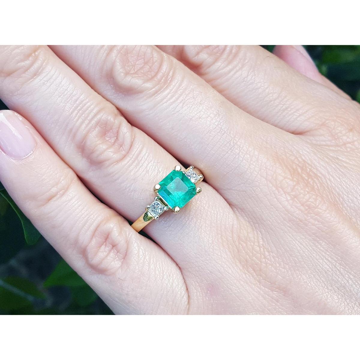 Emerald ring on a finger with a blurred green background.