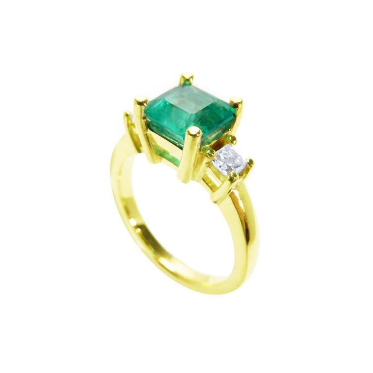 This 18k yellow gold three stone emerald ring is on a tilted position to show the top stone and side diamond profile.