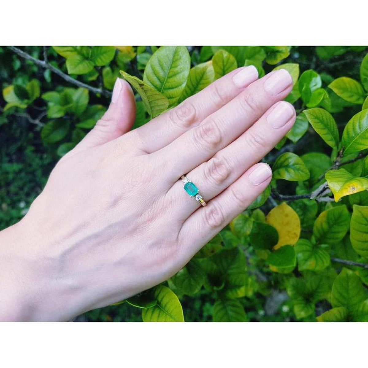 1.01 ct rectangular bluish-green emerald ring with natural diamond accents set in 14K yellow gold on a hand.