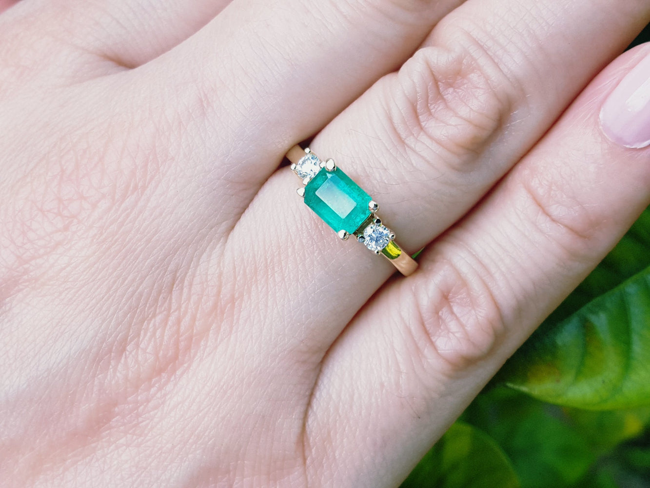 Emerald three stone ring on a hand with a blurred green background