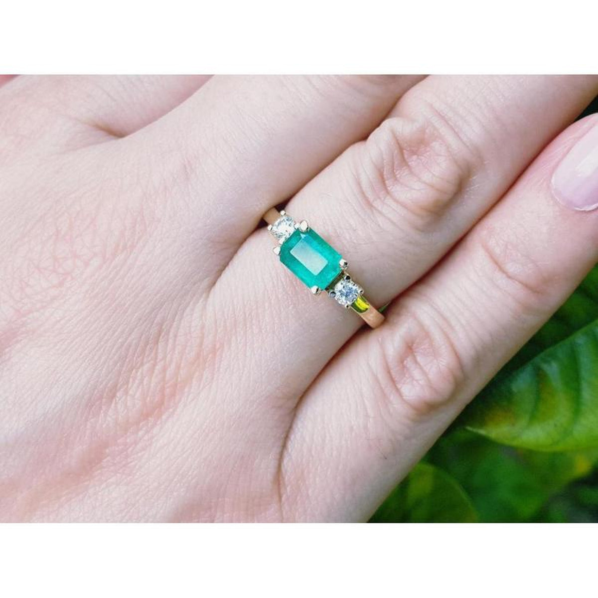 1.01 ct rectangular emerald ring with two diamond accents set in 14K yellow gold on a hand.