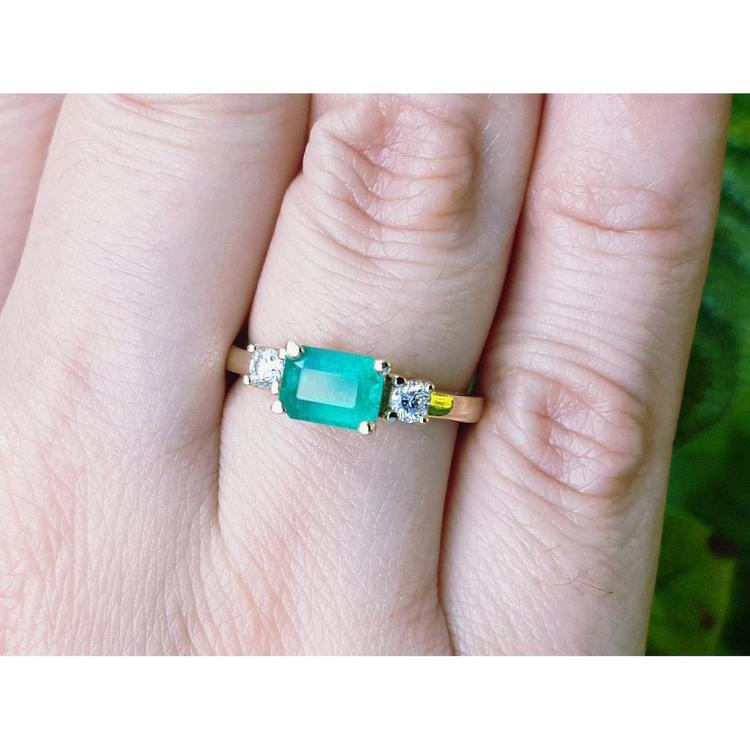 A 14k yellow gold emerald three stone ring with side diamonds on a person's finger.