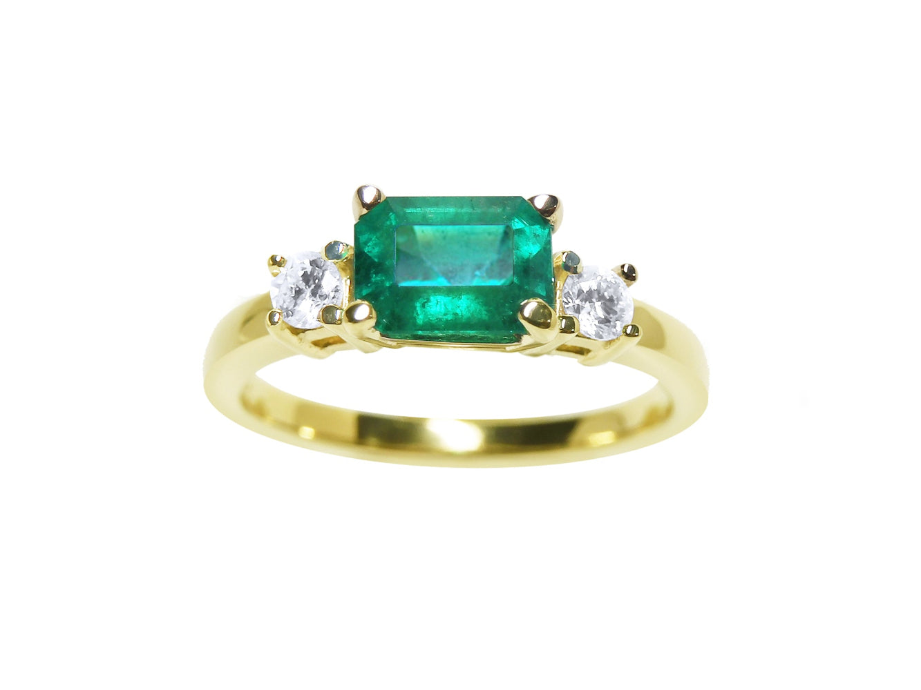 The topside of this three stone emerald ring displays the main stone with side natural diamonds.