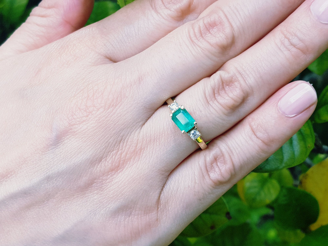 Hand wearing an emerald ring with a green leafy background