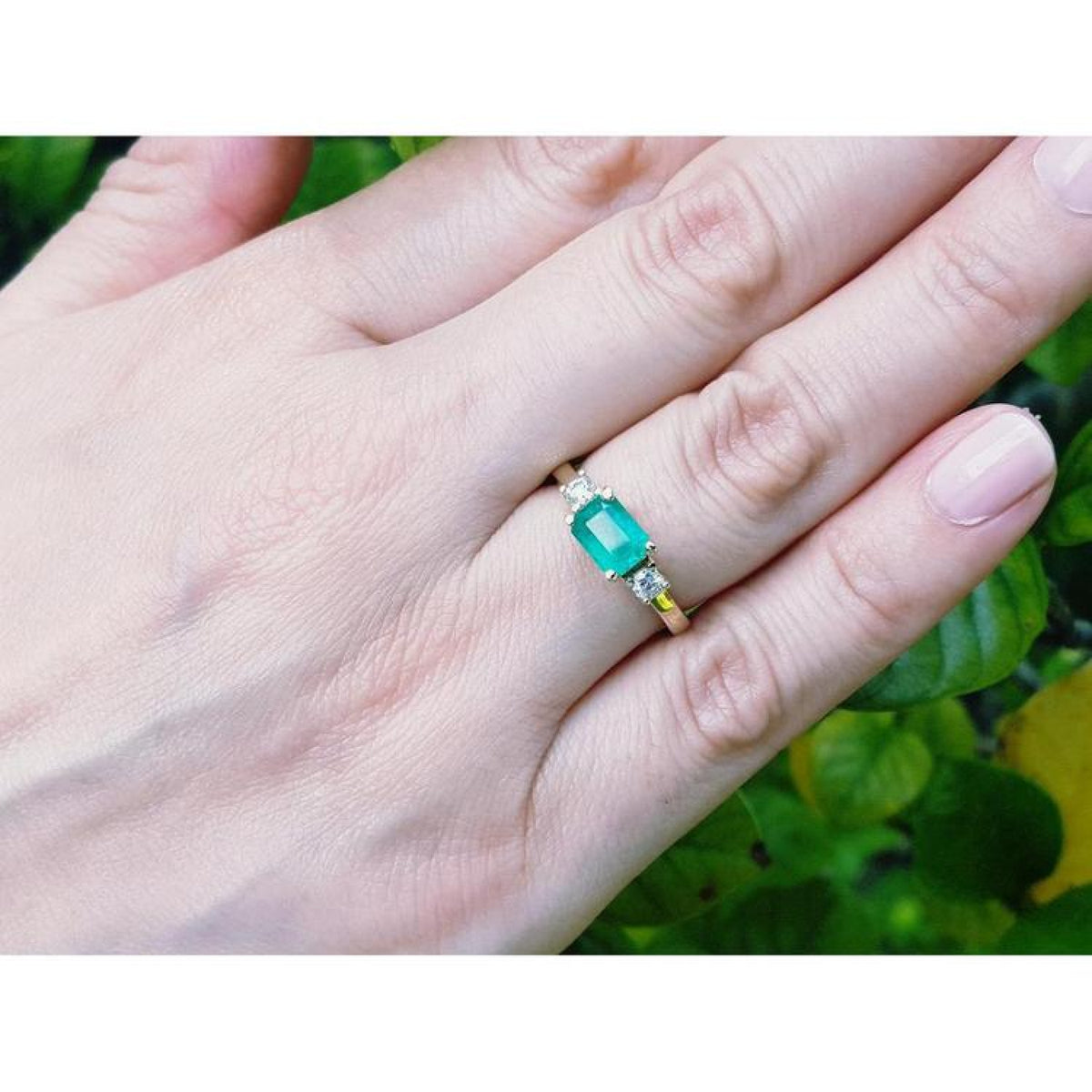 1.01 ct rectangular emerald ring with natural diamond accents set in 14K yellow gold on a hand.