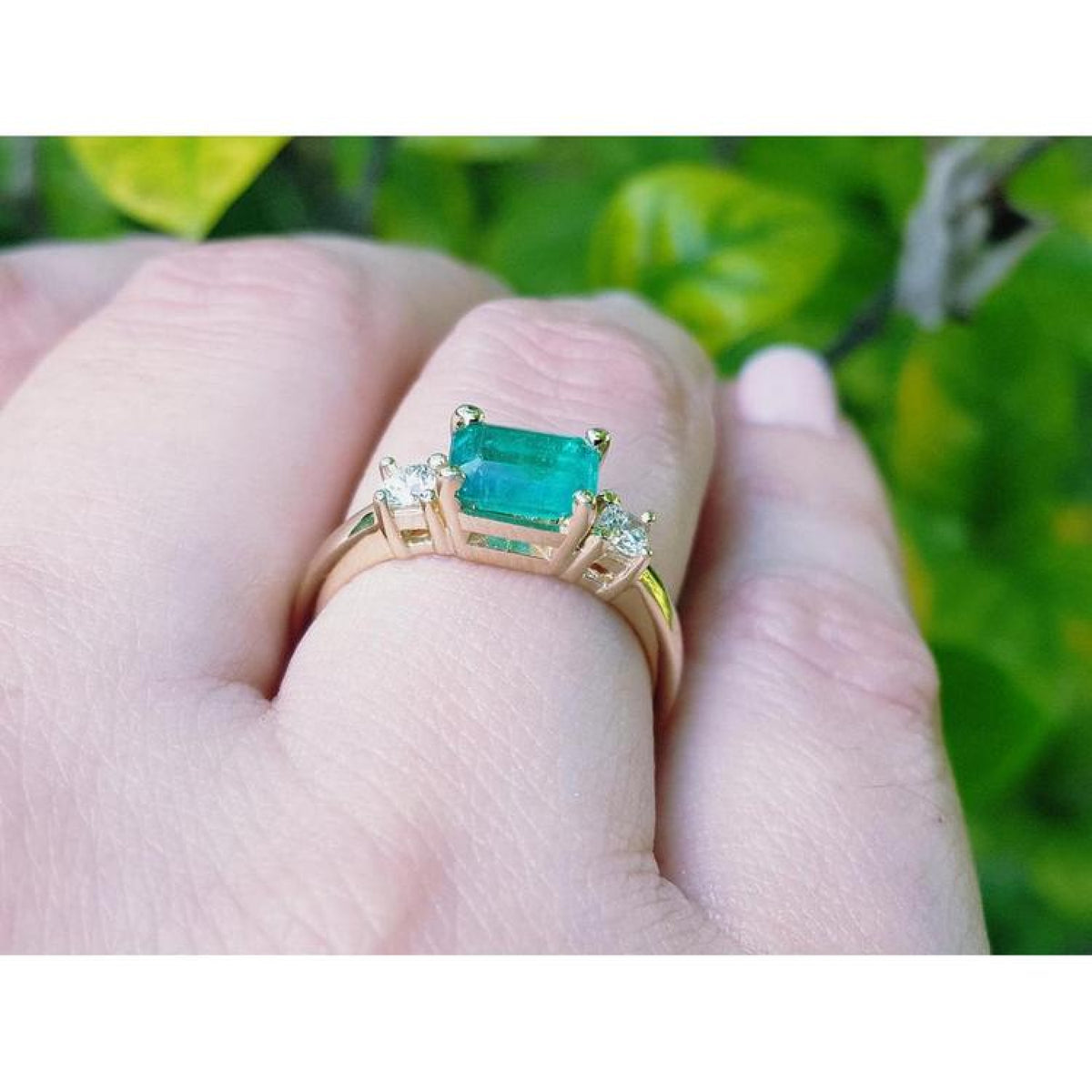 1.01 ct rectangular emerald ring with diamond accents set in 14K yellow gold on a finger.